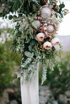 an arrangement of flowers and greenery is hanging from a pole