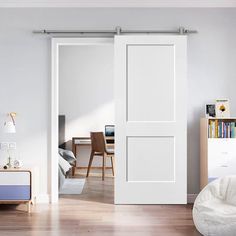 a bedroom with white walls and wooden floors, an open door leading to a living room