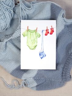 there is a card with clothes hanging on a line and two balls of yarn next to it