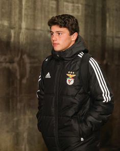 a young man wearing a black jacket and standing in front of a wall