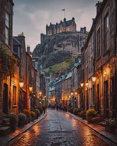 an empty street in front of a castle with lights on at the bottom and people walking down it