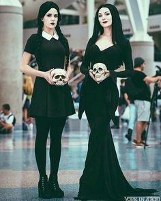 two women dressed in black holding skulls and posing for the camera with their hands on their hipss