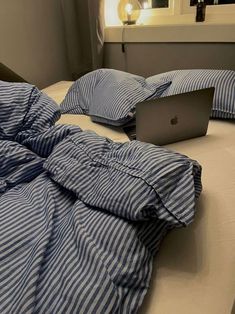 an apple laptop computer sitting on top of a bed covered in blue and white sheets