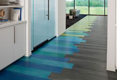 a long hallway with blue and green flooring next to a large window on the wall