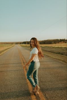 a woman riding a skateboard down the middle of an empty road with grass in the background