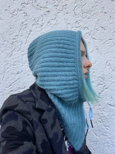 a woman with green hair wearing a blue knitted hoodie and looking off to the side