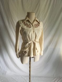 "vintage 1970s blouse Kendra of India imported by Interlines Inc. 100% cotton hand woven made in India natural white w/flecks button up long sleeve w/2 button cuff collared drawstring waist side to front w/non drawstring back band 2 front lower pockets w/flaps brown embroidered clovers on chest/pockets good vintage condition, light wear-light collar ring labeled M, see below measures, lying flat, shoulder-14 1/2\" sleeve-21 1/2\" chest-18 1/2\" waist w/drawstring open-16\" and w/drawstring pulled tightest-11\" hem-20\" length form top shoulder next to collar-22 1/2\"" Bohemian Fitted Collared Tops, Fitted Bohemian Collared Tops, Fitted Collared Bohemian Top, Fitted Collared Bohemian Blouse, Fall Bohemian Collared Blouse, Bohemian Style Embroidered Collared Top, Vintage Cotton Blouse For Festival, Bohemian Embroidered Collared Blouse, Vintage Long Sleeve Blouse With Boho Collar