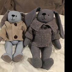 two stuffed animals sitting on top of a bed next to each other in sweaters