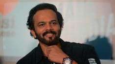 a man with a watch on his wrist smiling at the camera while wearing a black shirt