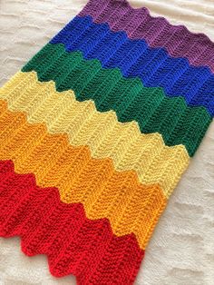 a multicolored knitted blanket laying on top of a white sheet with the colors of the rainbow in it