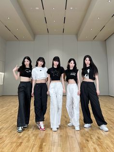 four girls in black and white outfits standing on a wooden floor