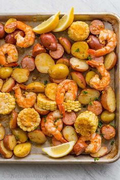 a pan filled with shrimp, potatoes and lemon wedges on top of a table