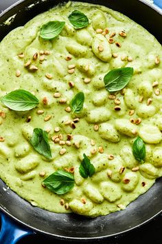 a pizza with pesto sauce and green leaves on top, sitting in a pan