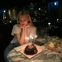 a woman sitting in front of a cake with lit candles on it at a table