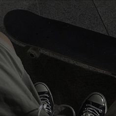 a person standing next to a skateboard on the ground with their feet propped up