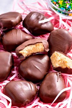 Close-up of homemade Reese’s peanut butter eggs on a pink shredded paper background, showcasing their rich chocolate coating and creamy peanut butter filling.