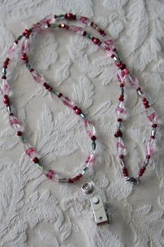 a pink and green beaded lanyard with a silver charm on a white surface