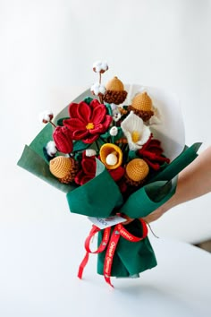 a person holding a bouquet of flowers on a white surface with red ribbon around it