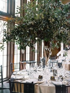 an elegant table setting with greenery in a tall glass vase on the centerpiece