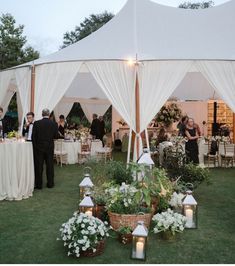 a group of people standing under a tent next to tables and chairs with flowers on them