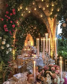 an outdoor dining area with candles and flowers on the walls, along with tables covered in white tablecloths