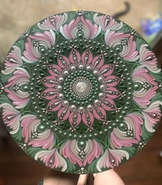 a hand holding a decorative plate with pink and green designs