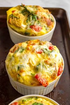 three small casserole dishes sitting on a baking tray, with broccoli and tomatoes in them