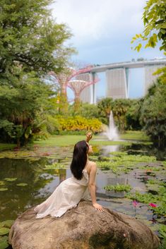 a woman sitting on top of a large rock next to a pond filled with water