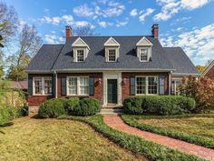 a brick house with green shutters on the front and side windows, surrounded by hedges