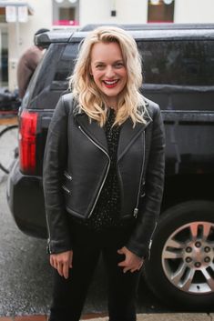 a woman standing in front of a black truck with her hands on her hips and smiling