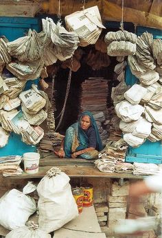 a woman sitting in the doorway of a building with stacks of papers hanging from it