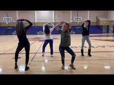 group of young women dancing on a basketball court with their arms in the air and one woman holding her head back