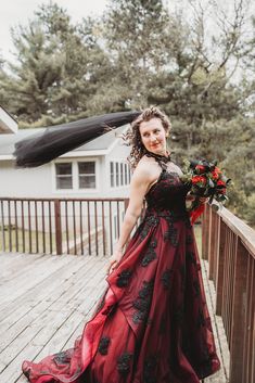 a woman in a red dress standing on a wooden deck with her veil blowing in the wind