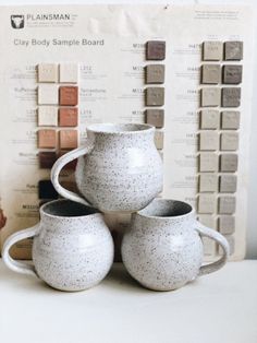 three white vases sitting next to each other on top of a table with paint samples in the background