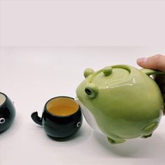 a hand holding a green teapot next to two black cups