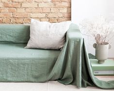 a couch covered with a green blanket next to a brick wall and potted plant