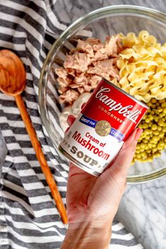 a person holding a can of soup in front of a bowl of pasta and vegetables