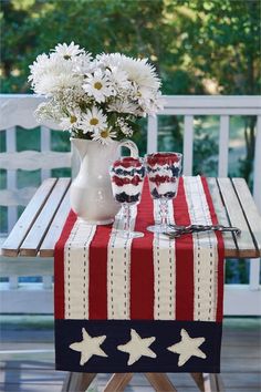 an american flag table runner with white daisies in a vase and two wine glasses