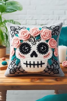 a crocheted skull pillow with roses on it sitting on a table next to a candle