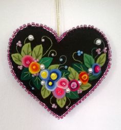 a heart shaped ornament with flowers and leaves on the front, hanging from a hook