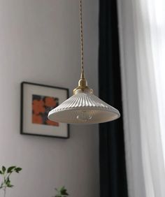 a white lamp hanging from a ceiling in a room with a potted plant next to it