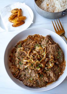 a white bowl filled with noodles and meat next to a pot of rice on a table