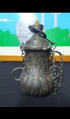 an old metal teapot with chains hanging from it's sides on a table