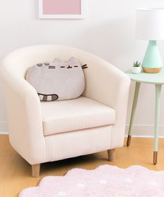 a cat pillow sitting on top of a white chair next to a pink table and lamp