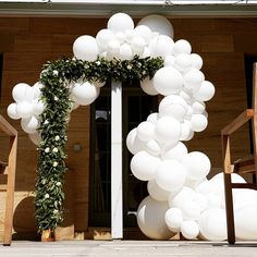 white balloons and greenery decorate the entrance to a house