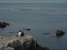 two people sitting on rocks near the ocean