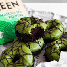 green chocolate covered doughnuts sitting on top of newspaper next to an open book