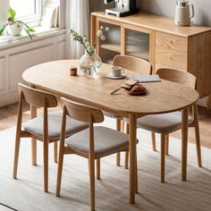 a wooden table with chairs around it in front of a window and vases filled with flowers