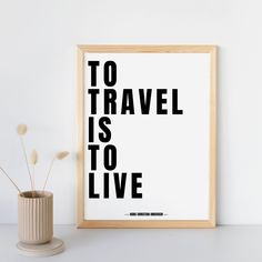 a black and white poster with the words to travel is to live on it next to a plant