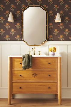 a wooden dresser with a mirror above it and flowers on the wall next to it